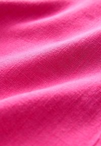 Tissu rose vif avec une texture tissée visible et des plis doux créant des ombres et des reflets doux.