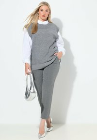 Suéter sin mangas gris sobre una camisa blanca con cuello, combinado con pantalones grises. Los accesorios incluyen un bolso de mano plateado y tacones metálicos.