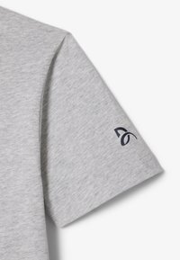 Camiseta gris claro de manga corta hecha de tejido suave, con un detalle del logo en azul marino en la manga. Diseño simple y limpio.