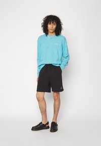 Light blue textured long-sleeve shirt, black shorts with drawstring, black slip-on shoes with a strap. Notable "obey" logo and Jordan detail.