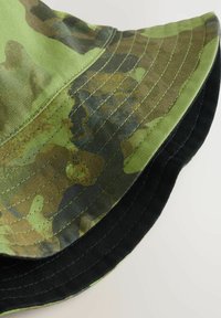 Grüner Camouflage-Eimerhut mit schwarzer Unterseite, aus leichtem Stoff gefertigt, mit sichtbaren Nähten und einem breiten, schlaffen Rand.