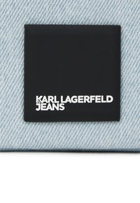 Gaišas zila džinsa audums ar melnu etiķeti, uz kuras ir izceltas baltas krāsas burti "KARL LAGERFELD JEANS". Kvadrātveida forma, gluda tekstūra.