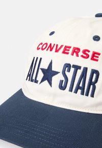 Fehér sapka kék karimával, a fronton piros és kék hímzett "CONVERSE ALL★STAR" felirattal és csillag díszítéssel. Texturált anyag.