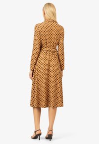 Langärmliges Kleid mit geometrischem Muster in Braun und Orange, mit einem taillierten Gürtel und einem fließenden Rock, aus leichtem Stoff gefertigt.