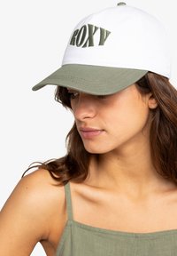 Gorra blanca y verde oliva con el texto "ROXY" bordado, diseño estructurado y visera curvada.
