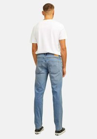 Jeans in denim azzurro chiaro con fit dritto, tasche posteriori e una piccola etichetta in pelle color beige sulla cintura. Abbinati a una t-shirt bianca.