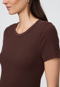 Brązowy prążkowany t-shirt z okrągłym dekoltem i krótkimi rękawami. Materiał jest miękki o teksturowanym wyglądzie. Wykończone brzegi przy rękawach.