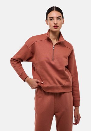 Sweatshirt zippé de couleur rose avec un col haut, des poignets côtelés et un tissu texturé. Présente une coupe décontractée et des détails sur les coutures latérales.
