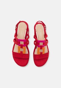 Sandales en daim rouge avec un design de lanières croisées, ornées d'accents géométriques multicolores en rose, orange et marron sur le dessus du pied.