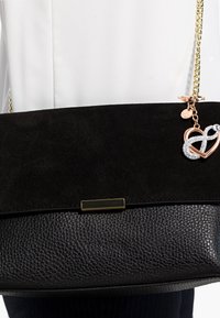 Borsa nera con fondo in pelle testurizzata e parte superiore in morbido suede. Manico a catena dorata e charm con un design a cuore e simbolo dell'infinito.