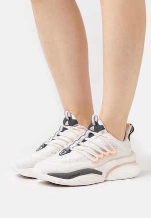 Zapatillas deportivas blancas con un upper texturizado, detalles en gris y rosa, y una suela acolchada marcada como "ADIPRENE" para soporte y comodidad.