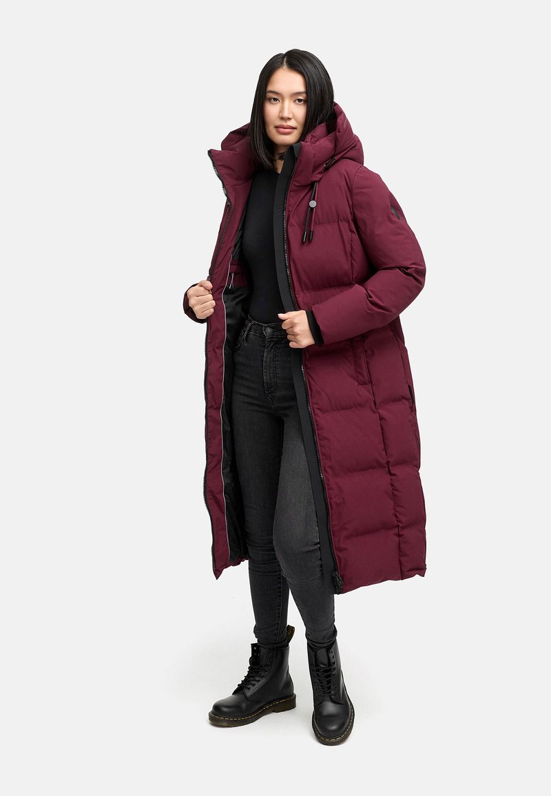 Bordeaux kleurige pufferjas met een capuchon, lange ontwerp, ritssluiting en zwarte accenten. Draag over een zwart top met donkere spijkerbroeken en zwarte laarzen.