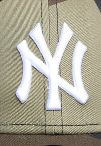 Tarnmütze mit einem auffälligen, weißen, gestickten NY-Logo. Hergestellt aus robustem Stoff mit einer strukturierten Oberfläche und kontrastierenden Nähten.