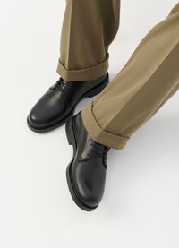 Zapatos de dress de cuero negro con un acabado suave, con cordones y punta redondeada, combinados con pantalones caqui arremangados.