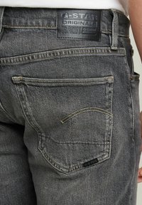 G-Star RAW grijze denim jeans met een leren taillebandpatch, voorzien van twee achterzakken en gele stikdetails.