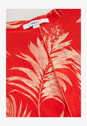 Czerwona tkanina teksturowa z off-white wzorami liści, z centralnym szwem i metką oznaczoną "NEXT" przy dekolcie.