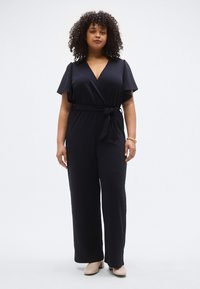 Tengerészkék, átlapolt stílusú overál rövid, fodros ujjakkal, öves derékkal és bőszárú nadrággal. Sima anyag, puha tapintású.