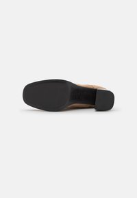 Suela de zapato de cuero con una parte inferior negra lisa y un empeine beige con detalles perforados. Tacón cuadrado para mayor estabilidad.