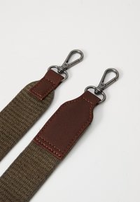 Brown fabric strap with leather accents and metal clips. Textured surface, sturdy design, and stitching detail on leather patches.