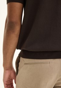 Dark brown knitted short-sleeve top with a ribbed hem, paired with light beige trousers featuring a sleek back pocket detail.