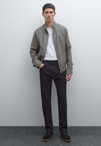 Brun texturerad bomberjacka över en vit t-shirt, ihop med mörka jeans och bruna skor. Enkelt design med minimal detaljering.