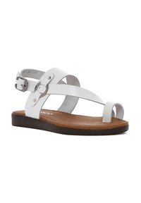 Sandalia de cuero blanco con tiras cruzadas y hebilla ajustable. Suela plana marrón con textura suave y diseño de punta abierta.