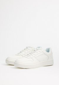 Zapatillas de piel blanca con una textura suave, puntera redonda, cierre de cordones en la parte delantera y detalles interiores en azul claro. Disponen de una suela de goma estriada.