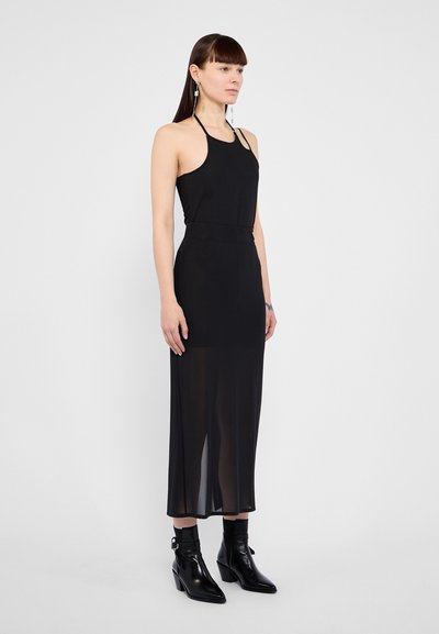 Black halter neck dress with a fitted bodice and sheer overlay, featuring a straight silhouette and ankle-length hem. Paired with black ankle boots.