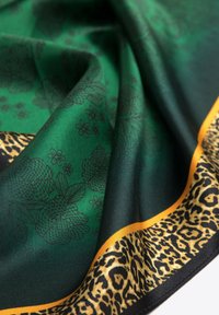 Groene zijde sjaal met een bloemenpatroon, omzoomd met een levendige gouden rand en een luipaardprint-sectie, die een gladde textuur laat zien.