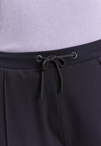 Donkerblauwe joggers hebben een gladde stof, een verstelbaar treklint met zwarte uiteinden, en een relaxed fit bij de taille en benen.