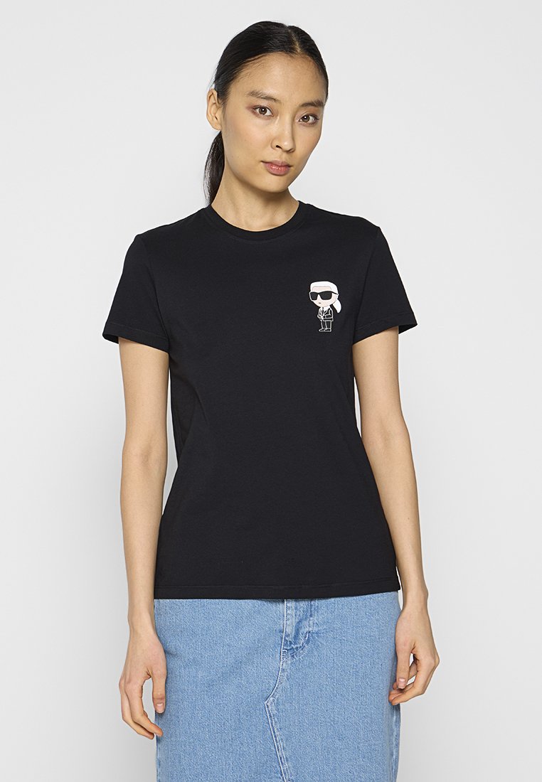 Schwarzes Baumwoll-T-Shirt mit kurzen Ärmeln und rundem Halsausschnitt. Verfügt über eine kleine weiße Cartoon-Grafik im Bereich der linken Brust.