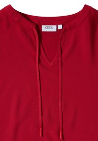 Blouse rouge pour femme avec col en V, cordons de serrage et une étiquette petite taille portant la mention "CECIL" à l'intérieur du col.