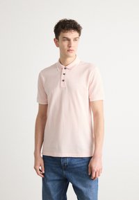 Ανοιχτό ροζ πόλο μπλούζα με δίπλο κουμπί, αντίθεση στο γιακά και κοντά μανίκια. Διαθέτει ένα μικρό λογότυπο στο αριστερό στήθος.