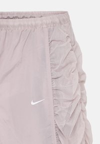Shorts Nike rose clair avec texture en maille froncée sur le côté et ceinture élastique. Comprend un logo Nike blanc sur le devant.