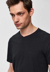 Camiseta negra de manga corta y escote en V, hecha de algodón suave. Presenta un corte relajado y un diseño minimalista sin patrones ni acentos visibles.