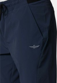 Pantaloni jogger blu navy realizzati in materiale morbido e leggero; presentano una vita elastica, un cordino e un logo ricamato a forma di ala sulla tasca.