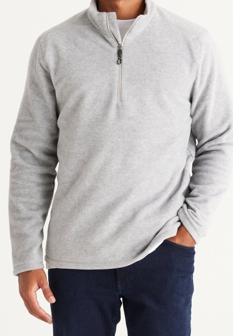 Grå fleecepullover med en halv-lynlås krave, der har lange ærmer og en blød tekstur. Kombineret med mørke jeans for kontrast.