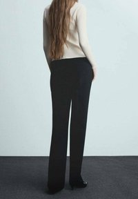 Czarne spodnie o szerokich nogawkach o gładkiej fakturze, zestawione z dopasowanym jasnym żebrowanym swetrem. Długie włosy modelki opadają na plecy.