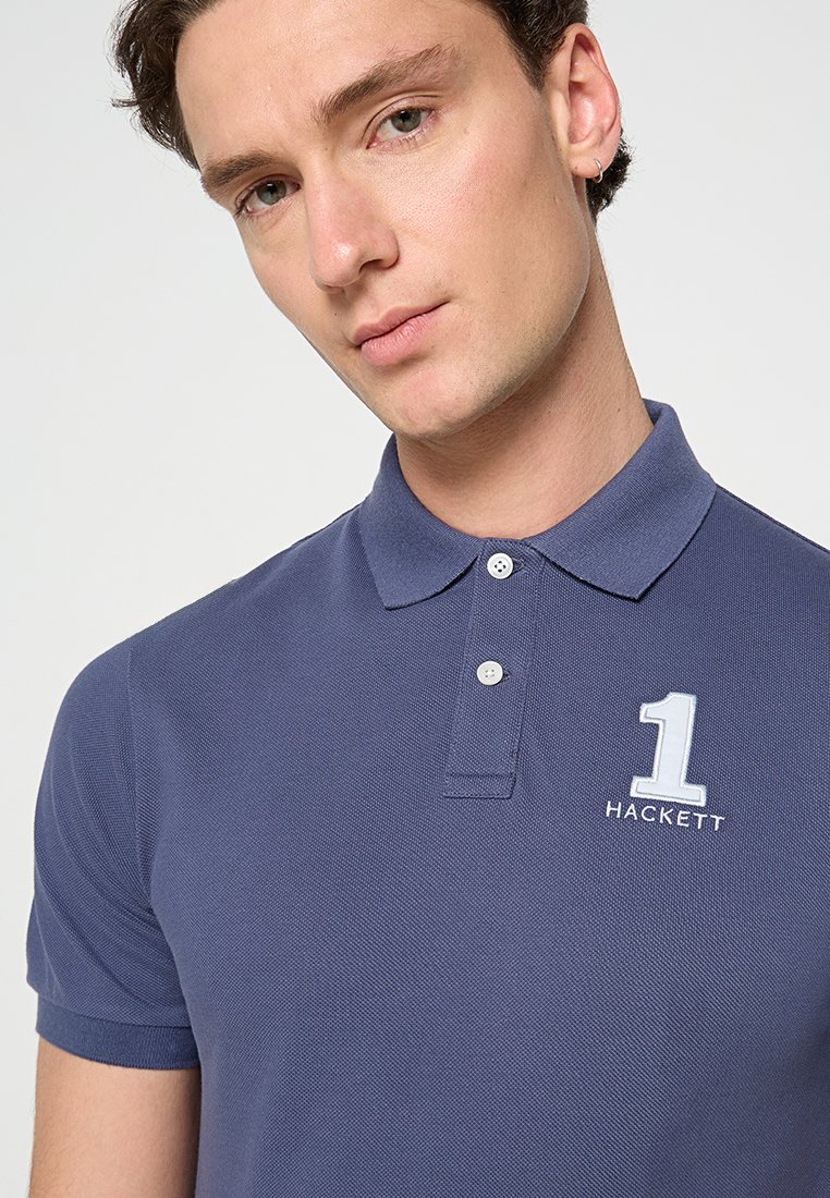 Polo bleu marine avec un tissu texturé, deux boutons au col, et un logo brodé blanc affichant le numéro 1 et "HACKETT."