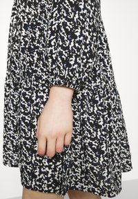 Svart klänning med ett strukturerat mönster av vita och blå prickar, med samlade ärmar och en utsvängd kjoldesign.