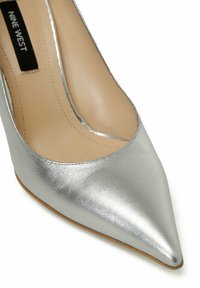 Zilveren hoge hak pump met een spitse neus en een gladde metallic afwerking. Interieur voorzien van beige voering. Merklabel: Nine West.