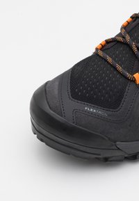 Svart tursko med en teksturert mesh-overdel og semsket skinn-detaljer. Har oransje lisser og en solid gummisåle med mønster. "FLEXTRON" detalj.