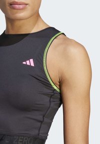 Gros plan sur une personne portant un haut de sport sans manches noir avec un logo rose et des coutures vert fluo le long de l'emmanchure.