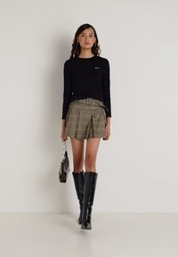 Fekete hosszúujjú felső, tompított árnyalatú kockás plissé rövidnadrág, széles öv, térdig érő fekete csizma, fémből készült kézitáskával.