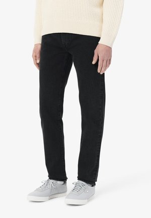 Jeans de mezclilla negra con un ajuste slim, que presentan un diseño clásico de cinco bolsillos y costuras sutiles. Llevados con unos zapatos de cordones gris claro.