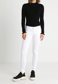 Top de manga larga negro acanalado, jeans ajustados blancos y zapatillas negras con suela blanca gruesa. Diseño sencillo, silueta ceñida.