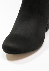 Schwarze Wildleder-Ankle-Boots mit runder Zehe und glatter Textur. Das Design zeichnet sich durch minimales Zubehör und einen niedrigen, verjüngten Absatz aus.