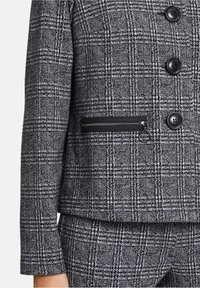 Blazer a quadri bianco e nero con una trama testurizzata, caratterizzato da una tasca con zip e chiusure a bottone. Design slim-fit con un look strutturato.