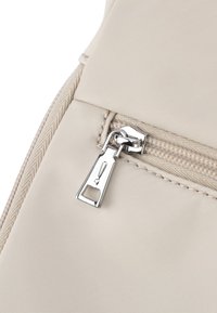 Borsa di tessuto beige con una cerniera argento e un tirante rettangolare, con cuciture testurizzate lungo l'area della cerniera.