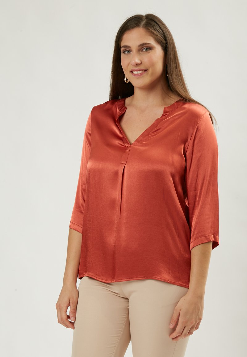 Satinorange Bluse mit V-Ausschnitt, dreiviertellangen Ärmeln und einem leichten Faltenwurf an der Vorderseite, mit glatter Textur und lässigem Schnitt.